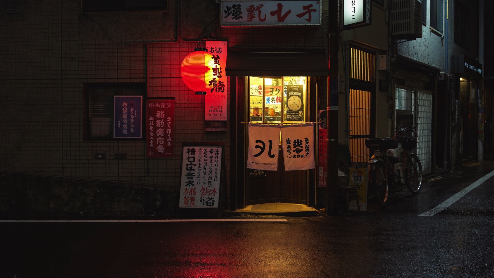 A narrow Japanese ramen alley at night, wet pavement glowing under a lit storefront with a red paper lantern and a noren curtain in the doorway